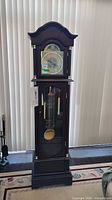 Full front view of the grandfather clock showing overall size, dark wood tone, pendulum and weights inside glass door.
