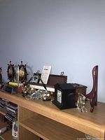 Wide view of entire lot on wooden shelf including clocks, horse figure, coasters, desk plaque, and boxed game.