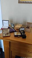 View of multiple jewelry items including wristwatches, cufflinks, pins, and rings in various boxes on a wooden surface.