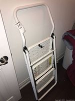 White metal framed folding step stool ladder with black anti-slip steps shown folded and unfolded.