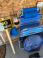 Side view of the folding Copa lawn chair featuring blue and white stripes with a padded headrest, next to the No Trespassing sign and blue storage bag below the chair.
