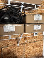 Three boxes with labels and electrical cords on a wire shelf in a garage setting, showing the lot contents.