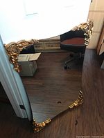 Full view of large flat mirror showing gilded corners and reflective surface.