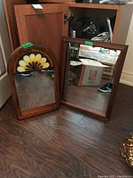 Two wood framed mirrors placed on floor. Rectangular mirror on right and arched decorative mirror on left, showing overall size and appearance.