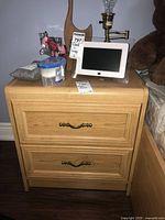 Wooden nightstand front view showing two drawers with brass handles and various items on top (not included).