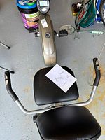 Top-down view of the recumbent bike showing padded seat with instruction manual, handlebars with pulse sensors, and the flywheel housing with the resistance knob and monitor.