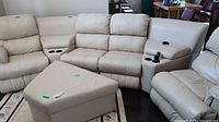 Four light beige leather sectional pieces arranged in living room with matching square ottoman