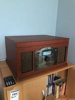 Full view of Crosley CR7002A stereo system in wooden cabinet sitting on shelf with remote control nearby.