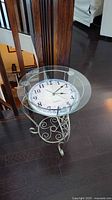Side view of glass top table showing built-in clock face and metal scrollwork base
