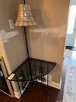 Full view of corner table with black glass top and attached lamp in corner against a wall.