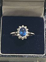 Ring in box showing frontal view of blue center stone with clear halo