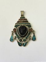 Front view of pendant showing stone face, inlay, and dangles