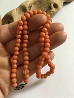 Coral bead strand held in hand, showing bead size, color and clasp