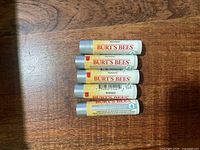 Five sealed Burt’s Bees Ultra Conditioning lip balms on wooden surface
