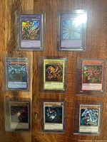 Eight Yu-Gi-Oh! cards in toploader sleeves on wooden surface