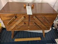 Closed antique wooden sewing box with medium-brown finish, wooden knobs, and fold-out arms visible.