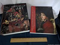 Two hardcover art history books side by side on a blue surface with a ruler for scale