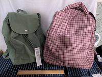 Photo of two backpacks: green canvas Palm + Perkins brand and pink checked polyester bag