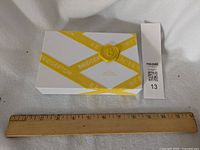 Closed Bridgerton collector's soap box with yellow branded ribbon and wax seal design next to ruler for size reference.