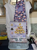 Wilton Cupcakes N More Dessert Stand boxed with floral baking aprons hanging