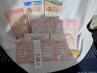 Photo showing multiple pink-packaged nail sticker packs with colorful designs, two nail art tattoo sticker packs, and false nails in packages with glue.
