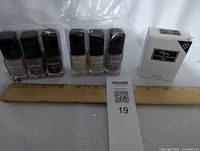 7 bottles of Lakur Enhanced Colour nail polishes displayed in a row next to a ruler, showing neutral beige and brown shades, unopened in original packaging.