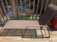 Side view of the adjustable brown outdoor lounge chair showing metal frame and fabric seating surface on a wooden deck.