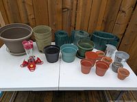Photo showing variety of planters, hummingbird feeder, and garden trim on white table against wooden fence