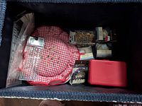 Blue fabric sewing basket containing sewing supplies and a red and white checkered pin cushion, small containers and boxes with needles, pins and other notions.