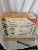 Boxed Dressmaker Sewing Center kit showing branding, sewing machine image, and accessory count with a ruler for scale.