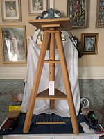 Full view of the solid wood sculpture stand showing tall height, square rotating top, four tapered legs, and triangular base platform.