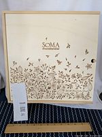 Top view of Soma Chocolatemaker wooden box showing engraved floral design and logo on sliding lid, with ruler for size reference.
