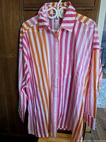 Front view of a large striped beach shirt with vertical stripes in orange, pink, red, and white, featuring a collar and breast pocket.