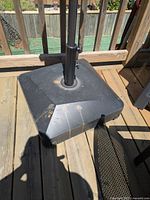 Black plastic and metal umbrella stand with central pole holder and visible wheels, showing some dirt marks.