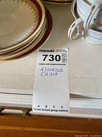 Close-up of assorted china dishes stacked showing gold-trim details and maroon border plates along with a few cups.