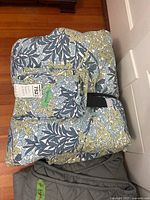 Queen bedding set folded showing green, blue, and white leaf pattern with label indicating queen size.