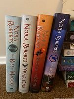 Four hardcover Nora Roberts books standing upright showing front covers with titles The Rise of Magicks, Year One, Blood and Bone, and Becoming.