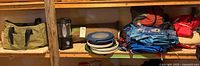 Shelves with green tent bag, Coleman lantern, camping plates, tarps, and other camping supplies