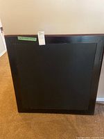 Folding wooden card table folded up, showing black surface and wood frame.