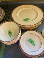 Stack of 10 dinner plates, 8 soup bowls, and some side plates with decorative gold and multi-color rim pattern.