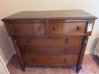 Front view of the wooden dresser showing five drawers, wooden knobs, and round column details on both sides.