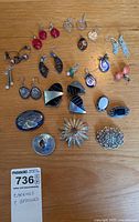 Full view of 21 earrings and 5 brooches arranged on wood surface.