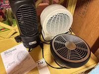 Three fans displayed including a black tower fan heater, a white circular fan heater, and a black circular oscillating fan all with power cables.