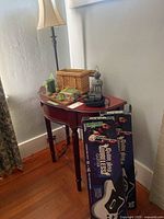 View of the small half-moon wooden side table with table lamp, binoculars, basket, lantern, and two Guitar Hero Wireless guitar boxes leaning against the wall