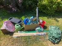 Full view of all garden items laid out on grass including planters, watering can, box with tools, fencing, netting, and bag