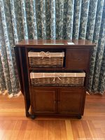 Full front view of wooden ironing board table showing foldable side, two wicker baskets, drawer, and cabinet doors.