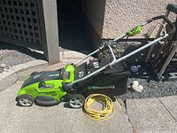 Side view of lawnmower showing green and black body, handlebar, wheels, grass collection bag and yellow extension power cord.