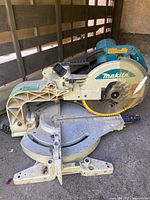 Side view of Makita mitre saw showcasing saw blade, handle, base with angle markings and body with Mekita branding