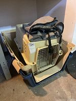 Stacked small and large plastic pet travel kennels with metal front doors, beige and dark blue colors. A folded black and gray fabric car seat cover lies on top.