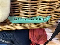 Close-up photo of the woven picnic basket showing a green label with dimensions W23 x 15 x H8.